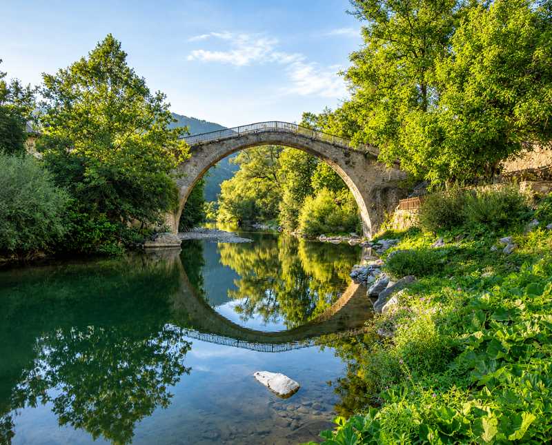 Παραδοσιακό πέτρινο τοξωτό γεφύρι στο Ζαγόρι που καθρεφτίζεται στο ποτάμι